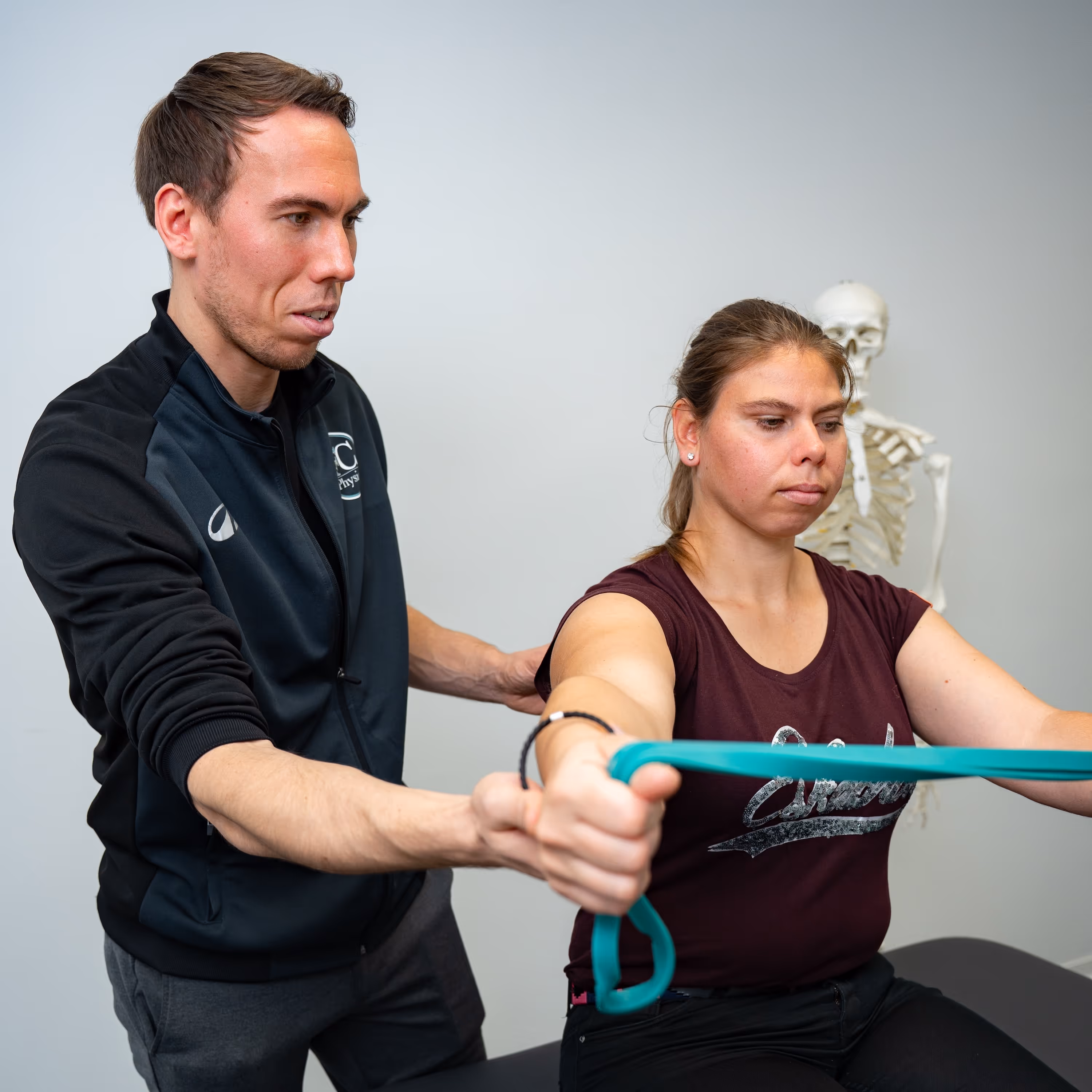 Krankengymnastik bei FC Physio: Physiotherapeut übt mit einer Patientin mit dem Theraband