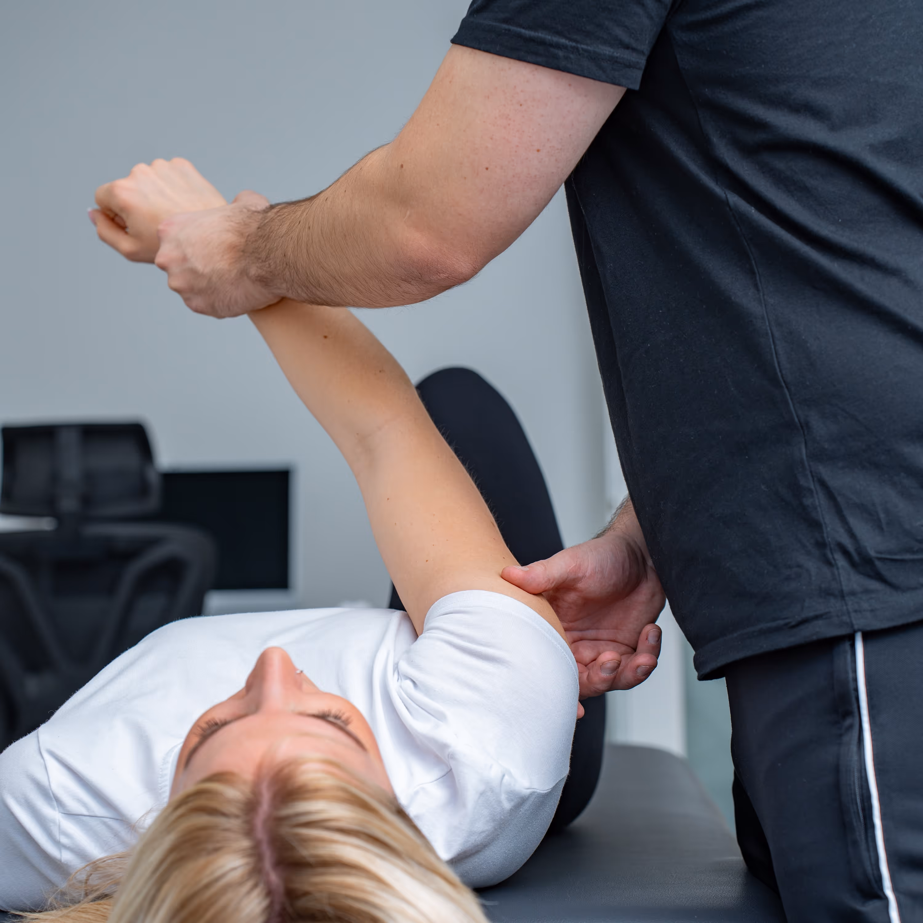 KG-ZNS nach PNF bei FC Physio: Physiotherapeut führt den Arm einer liegenden Patientin